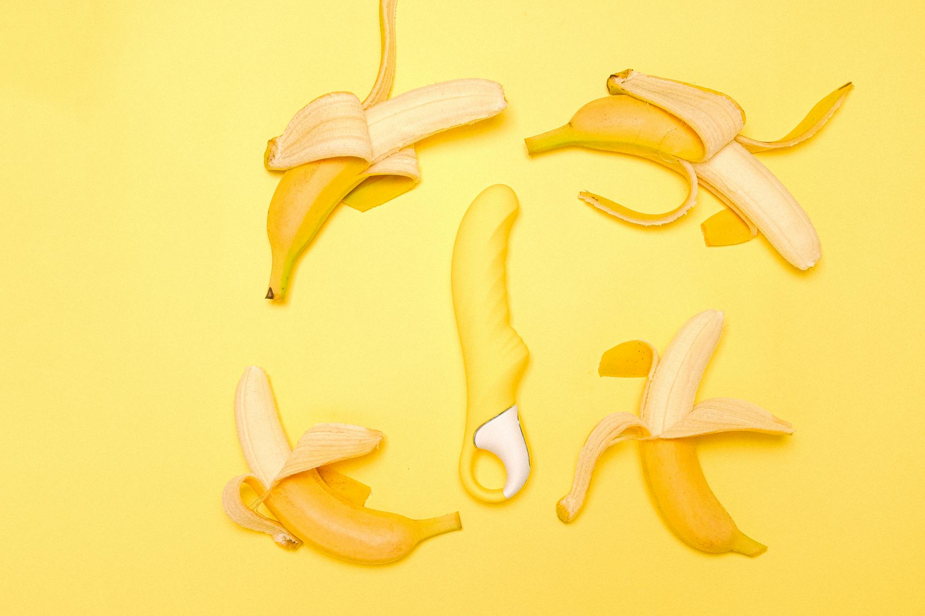 A yellow silicone lemon vibrator surrounded by fresh peeled lemons on a bright yellow background.