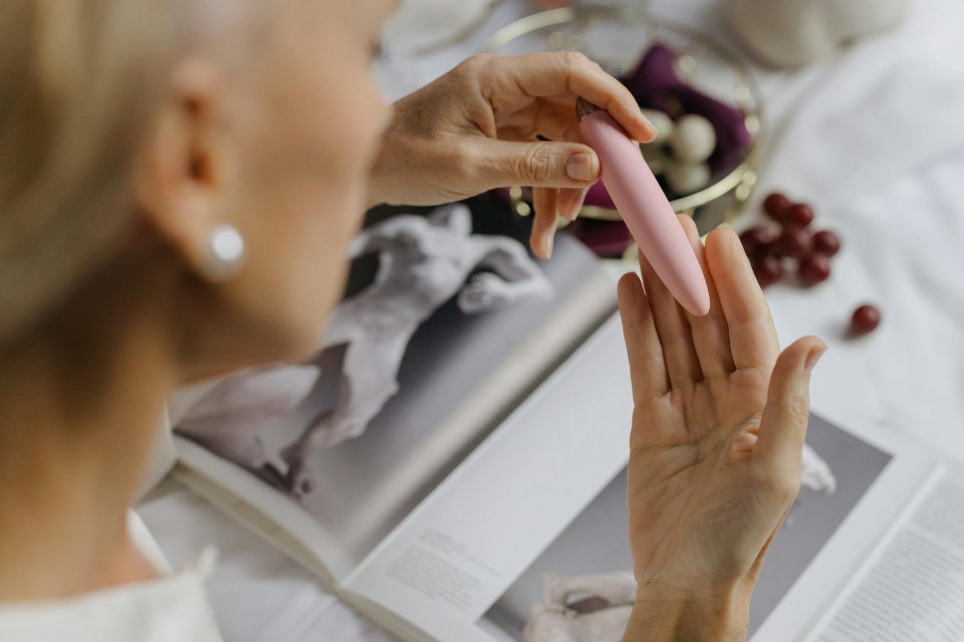 Woman holding a pink vibrator with books in the background, symbolizing the integration of pleasure and intellectual self-care.