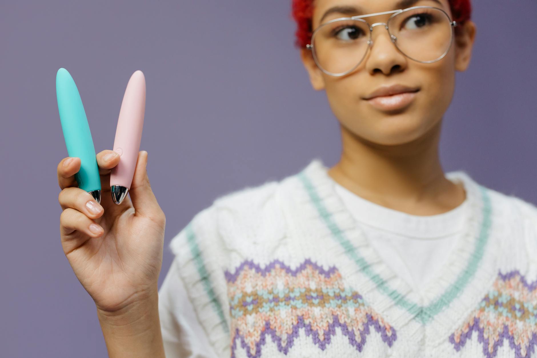 Woman holding colorful vibrators against a purple background, representing pleasure and sexual wellness.
