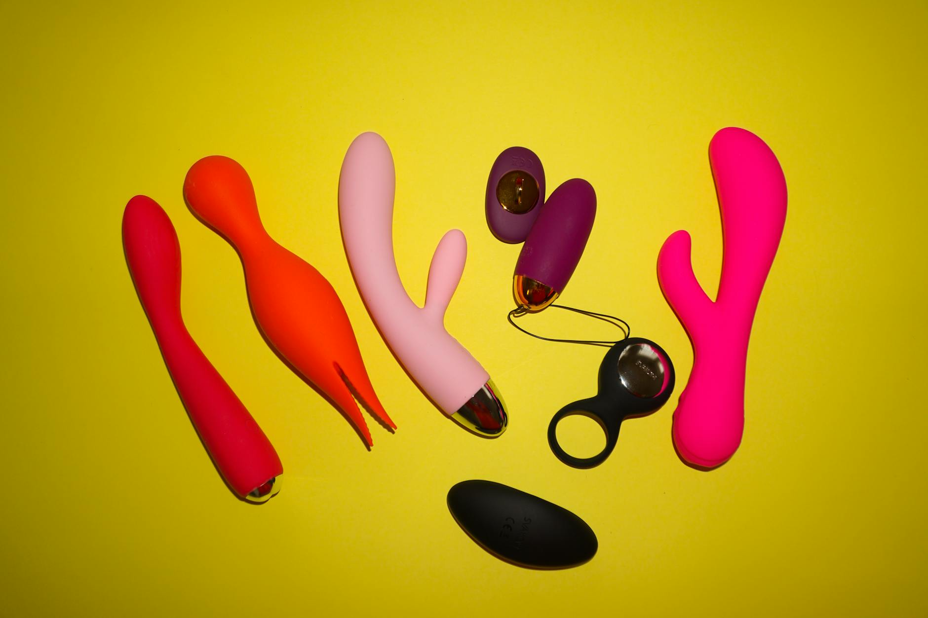 Colorful sex toys arranged on a bright yellow background, including vibrators and massage devices